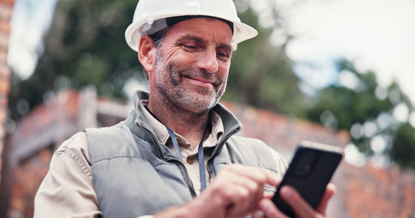 Contractor in a hard hat smiling at his phone on a building site