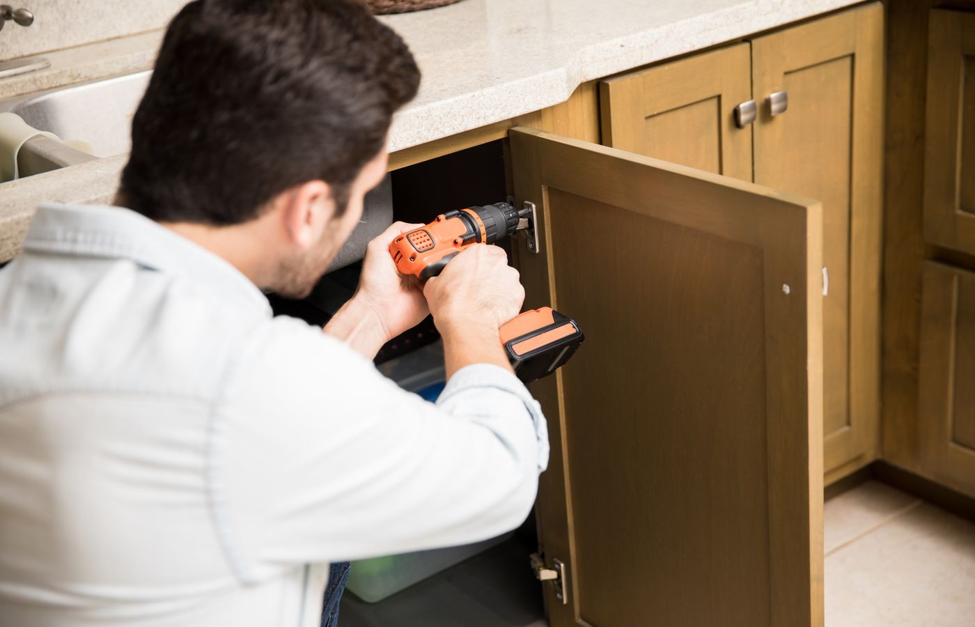 Contractor fitting a kitchen cabinet door with a drill