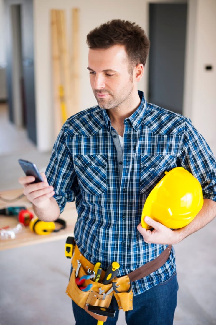 Tradesman with a tool belt and hard hat using his phone